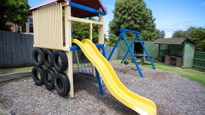 A playground with a yellow slide, a tire play structure, and a swing set.