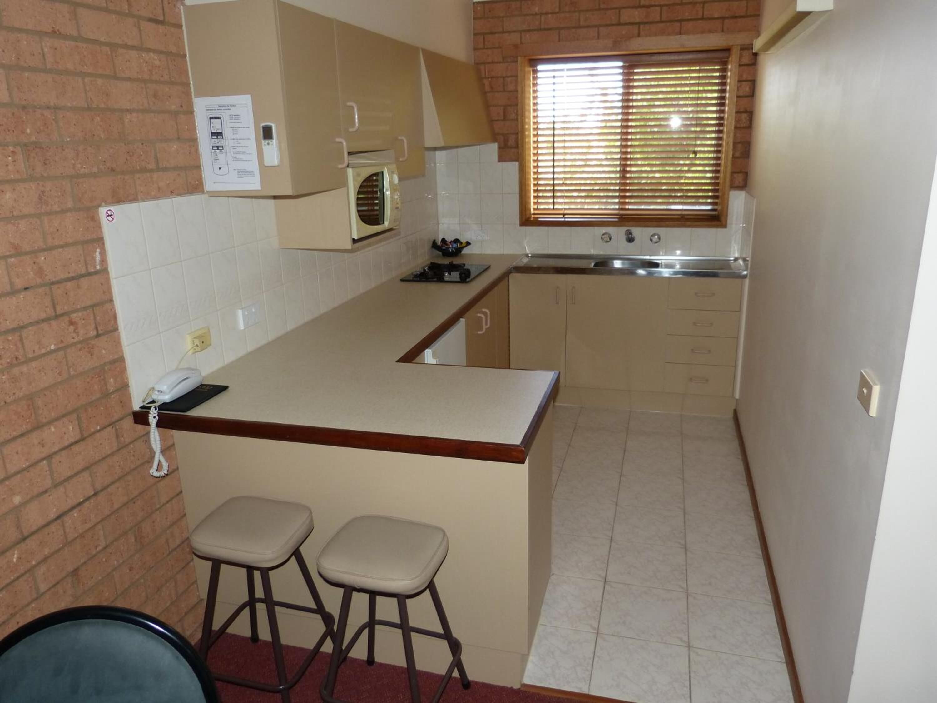 Una cocina compacta con una pequeña isla, un microondas y una ventana con persianas.