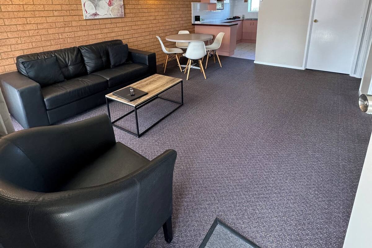 A modern living room with a black leather sofa, a coffee table, and a dining area with a small island and chairs.