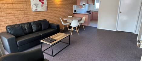 Un salon moderne avec un canapé en cuir noir, une table basse et un coin repas comprenant un petit îlot et des chaises.