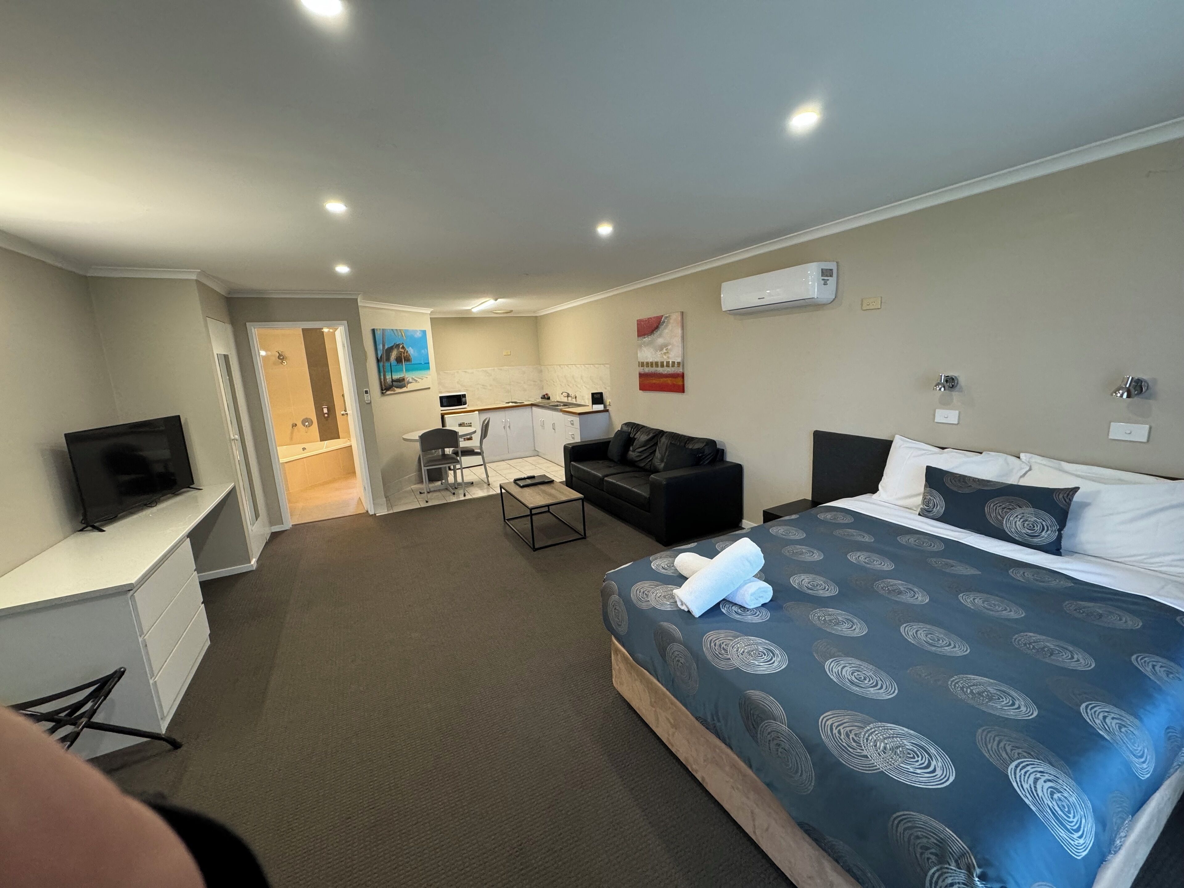 A hotel room with a bed, a desk, a chair, a sofa, and a television.
