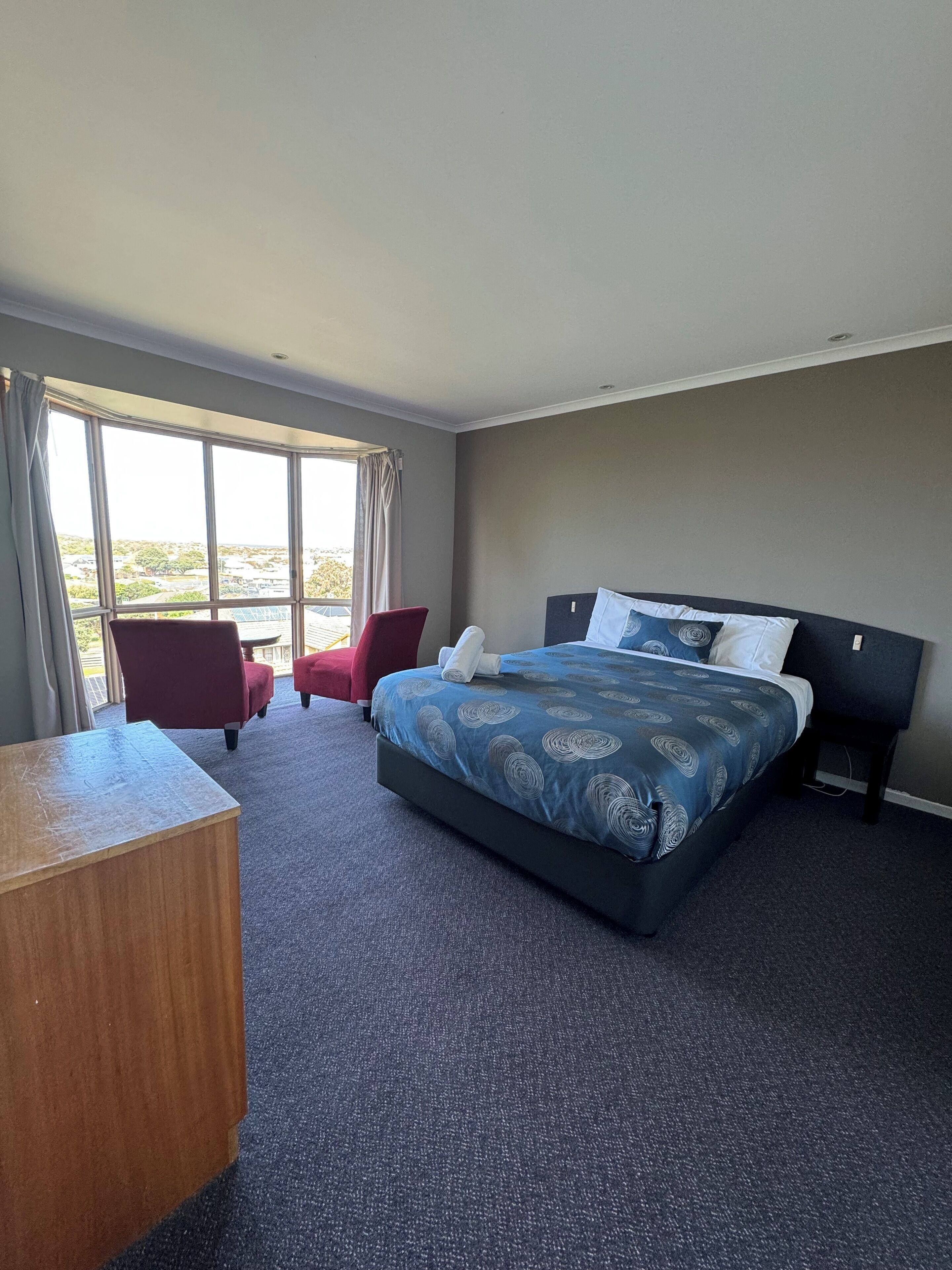 A hotel room with a large bed, a desk, a chair, and a view of the outdoors.