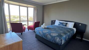A hotel room with a large bed, a desk, a chair, and a view of the outdoors.