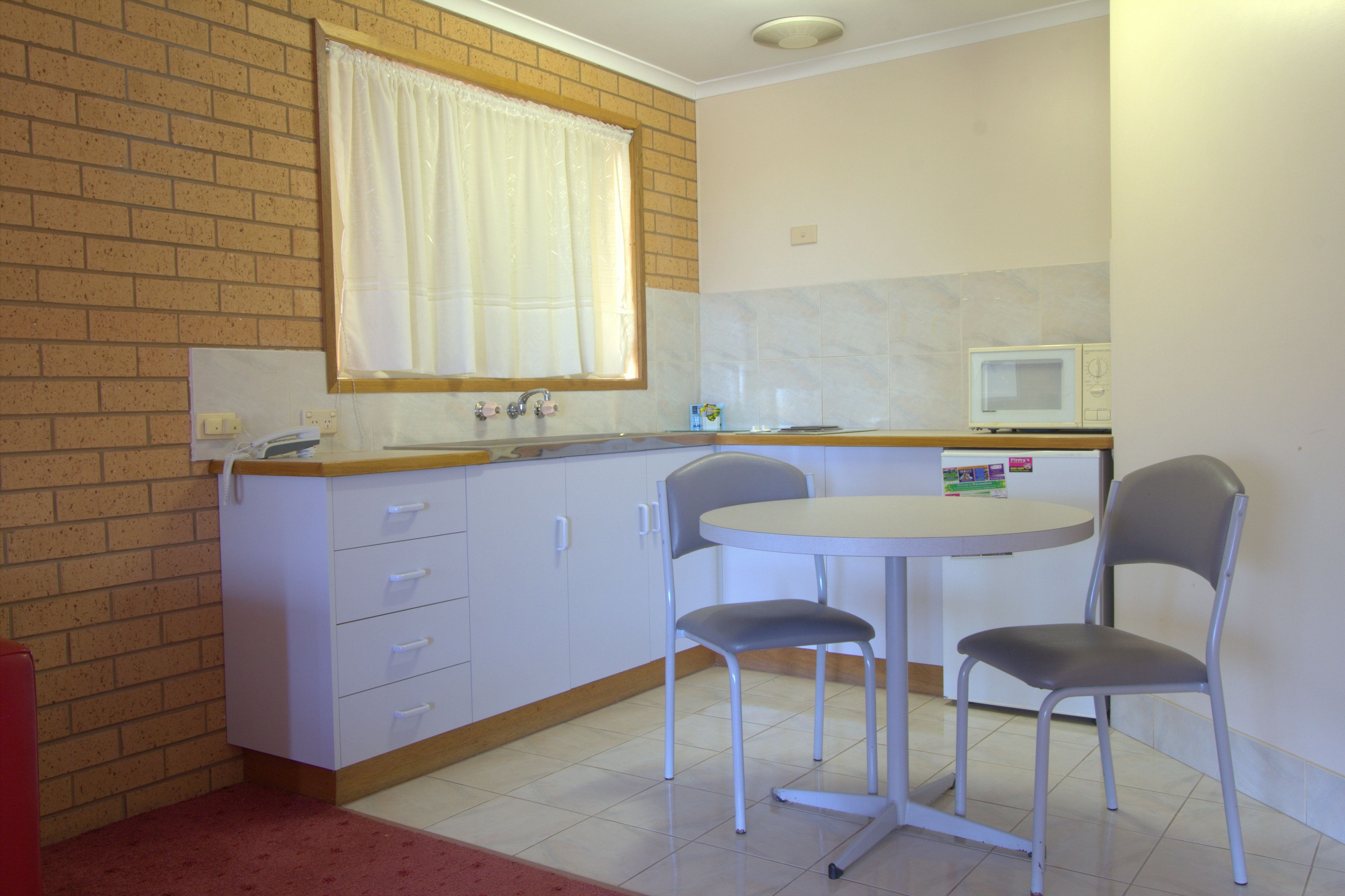 A small kitchen with a sink, a microwave, two chairs, and a window with a curtain.