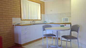 A small kitchen with a sink, a microwave, two chairs, and a window with a curtain.