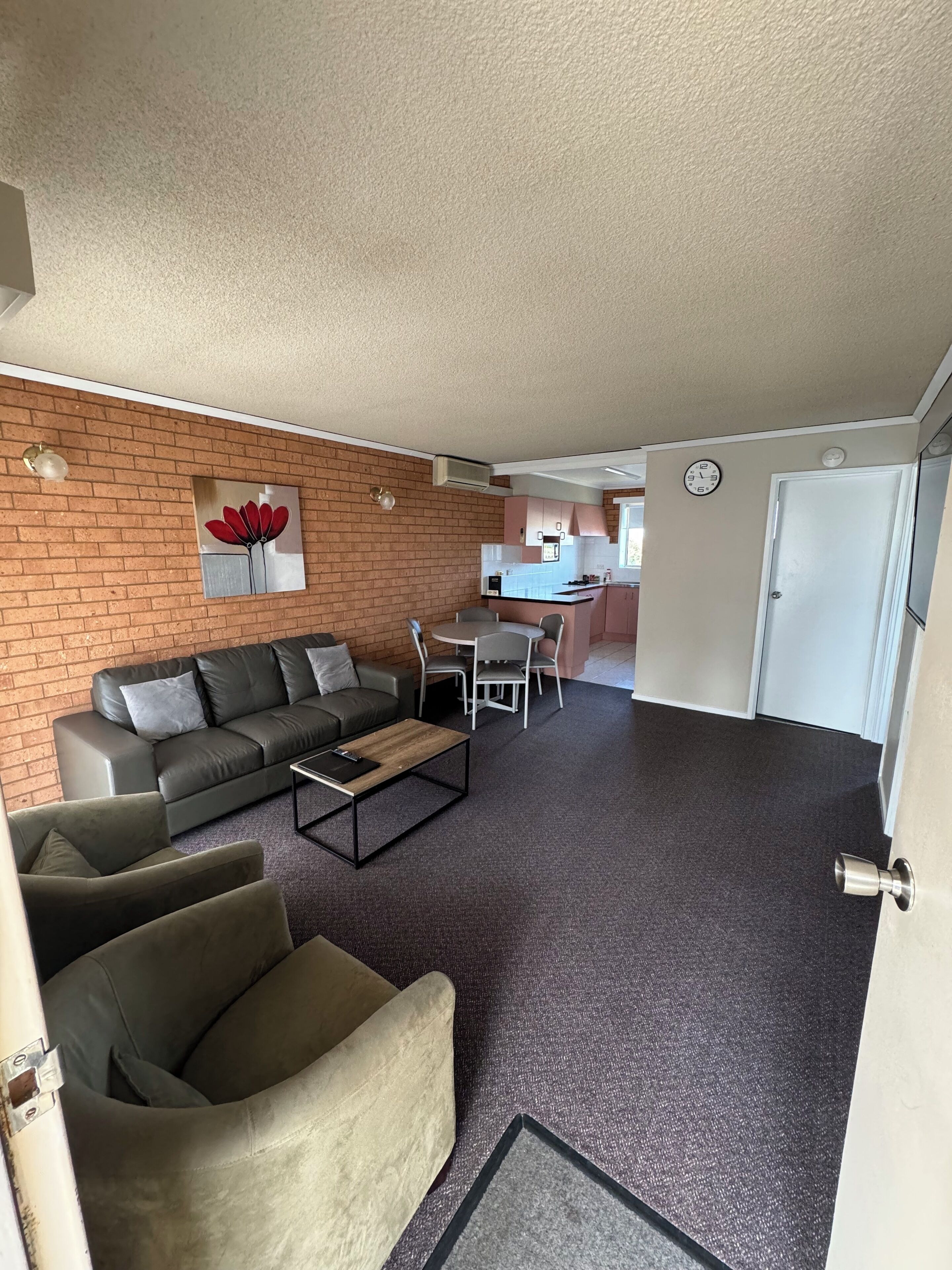 A modern living room with a brick wall, a sofa, a coffee table, and a dining area with chairs.