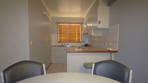 A compact kitchen with a dining area, featuring a small island, a sink, and a window with blinds.