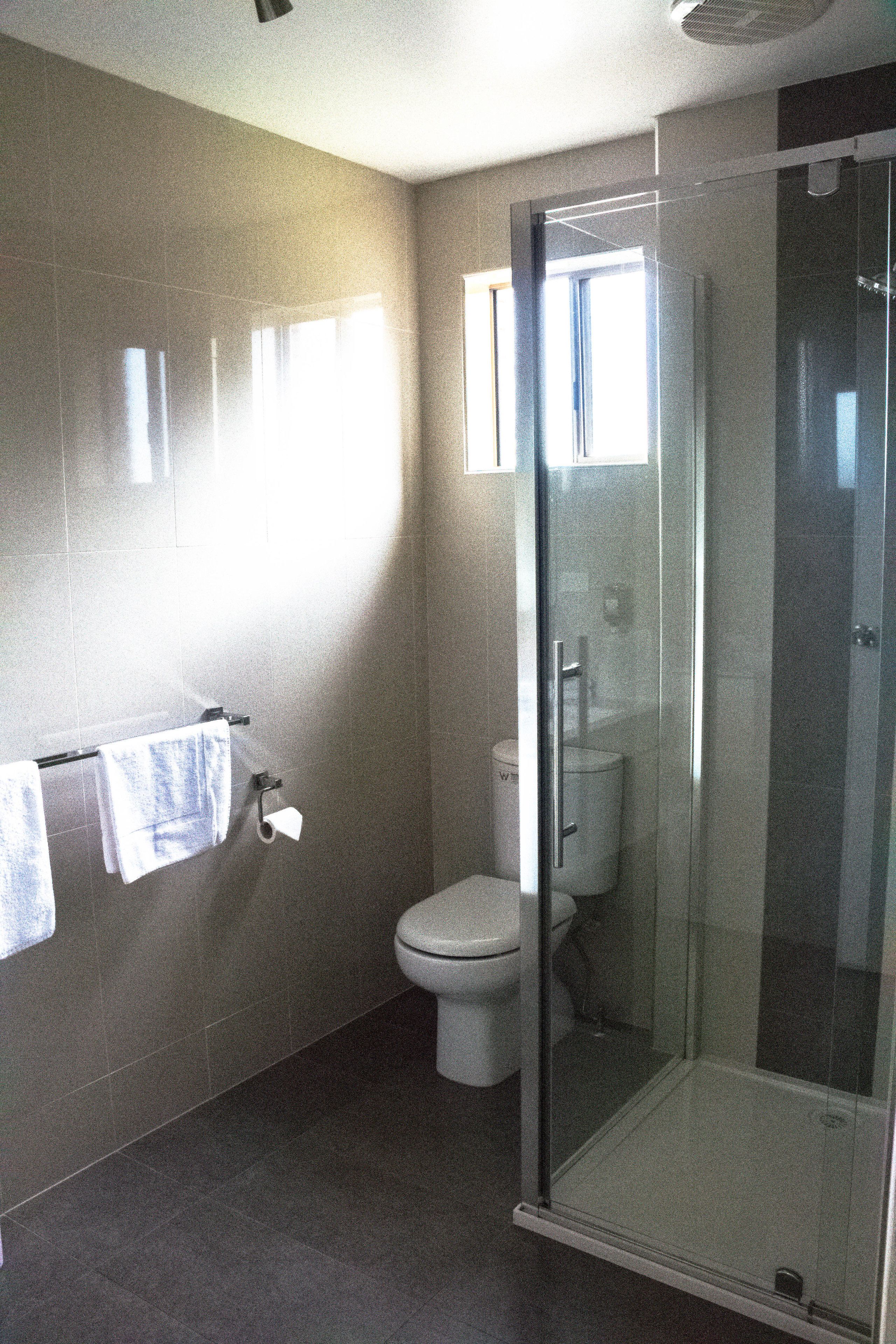A bathroom with a glass-enclosed shower, a toilet, and a towel rack with towels.