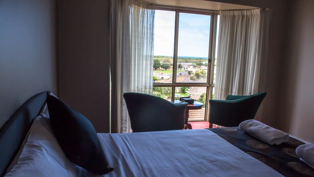 A hotel room with a large bed, two chairs, a small table, and a view of the outside.