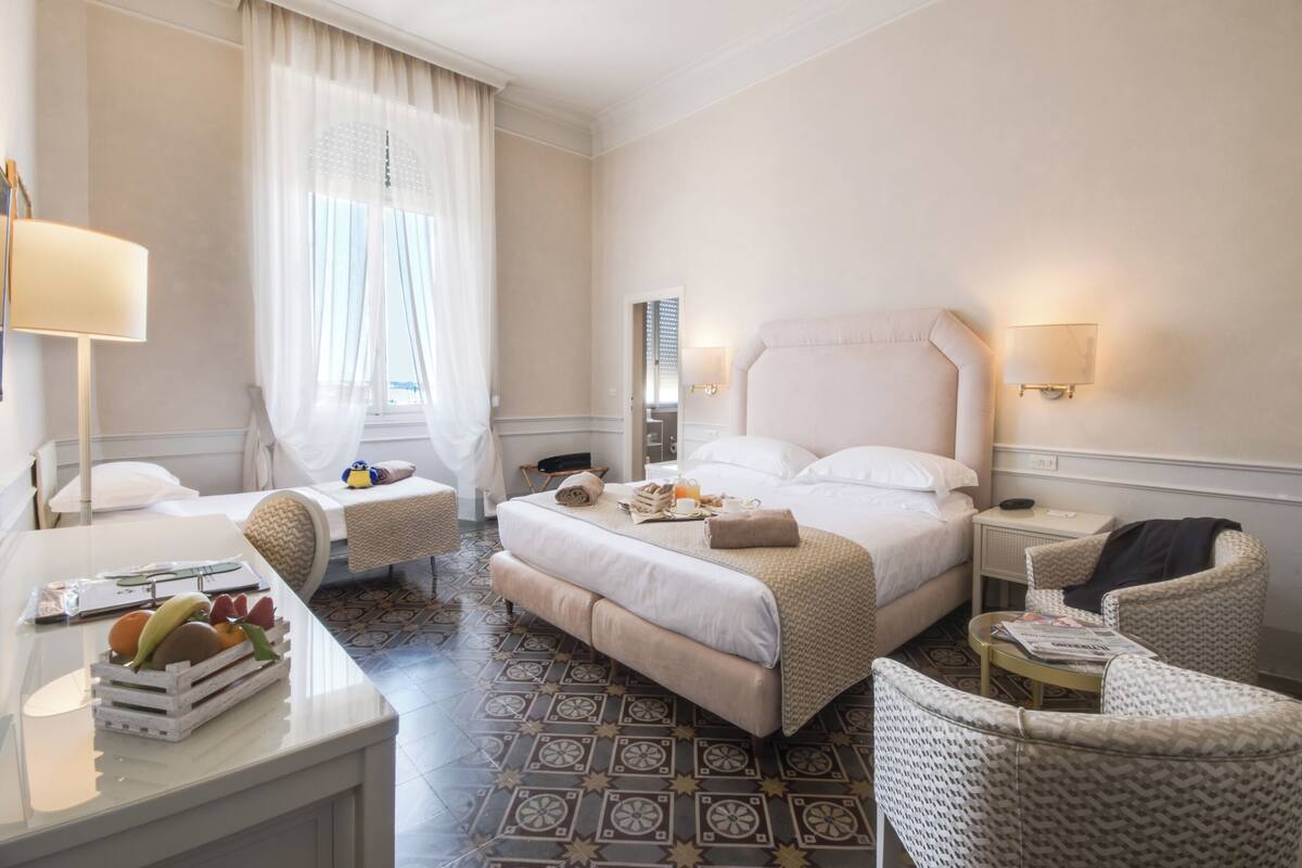 A hotel room with a bed, bedside tables, a desk, a chair, and a dining area.
