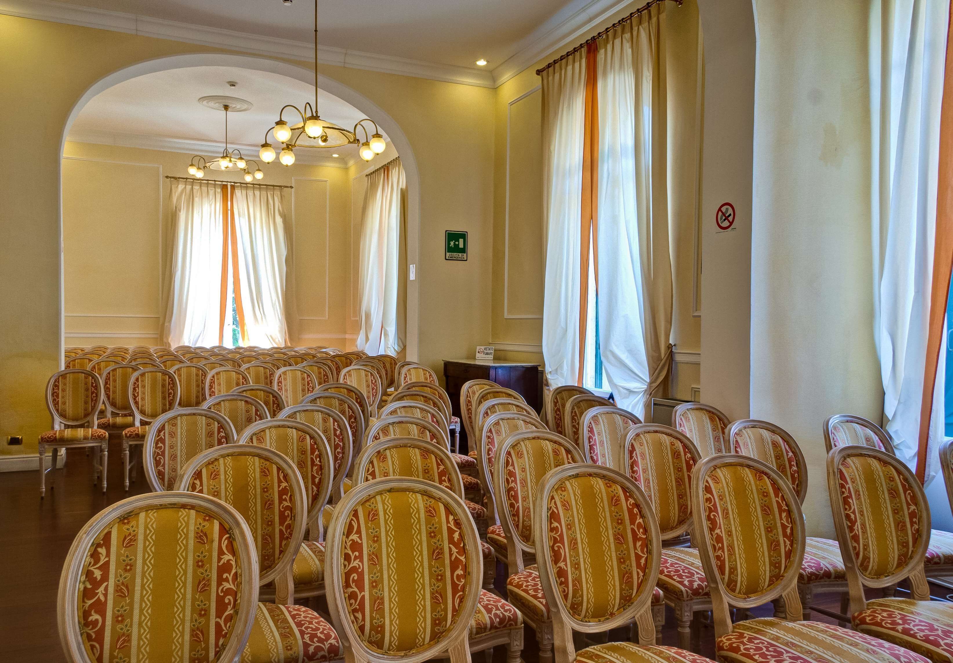 Ein Konferenzraum mit Stuhlreihen, einem Chandelier und Vorhängen.