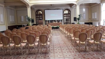 Una sala conferenze con file di sedie, un palco con uno schermo e una moquette decorata.