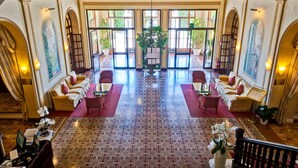 A spacious lobby with a patterned floor, two sofas facing a central plant, and a chandelier. - Grand Hotel Royal (Viareggio)