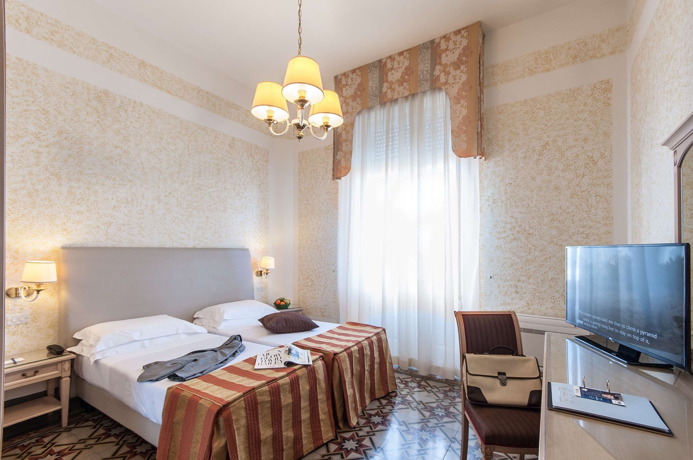 A hotel room with a bed, bedside table, lamp, TV, and a chair.