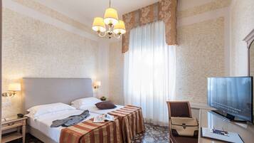 A hotel room with a bed, bedside table, lamp, TV, and a chair.
