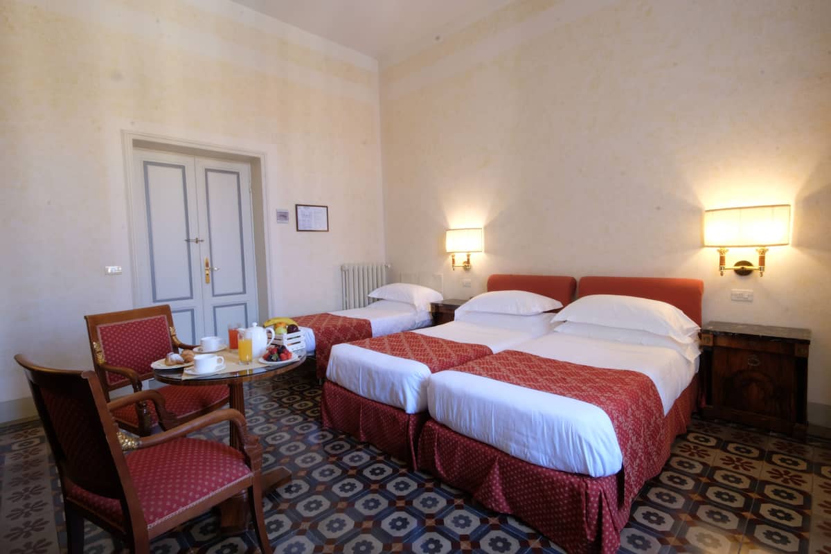 A hotel room with two beds, a dining table with breakfast, and a chair.