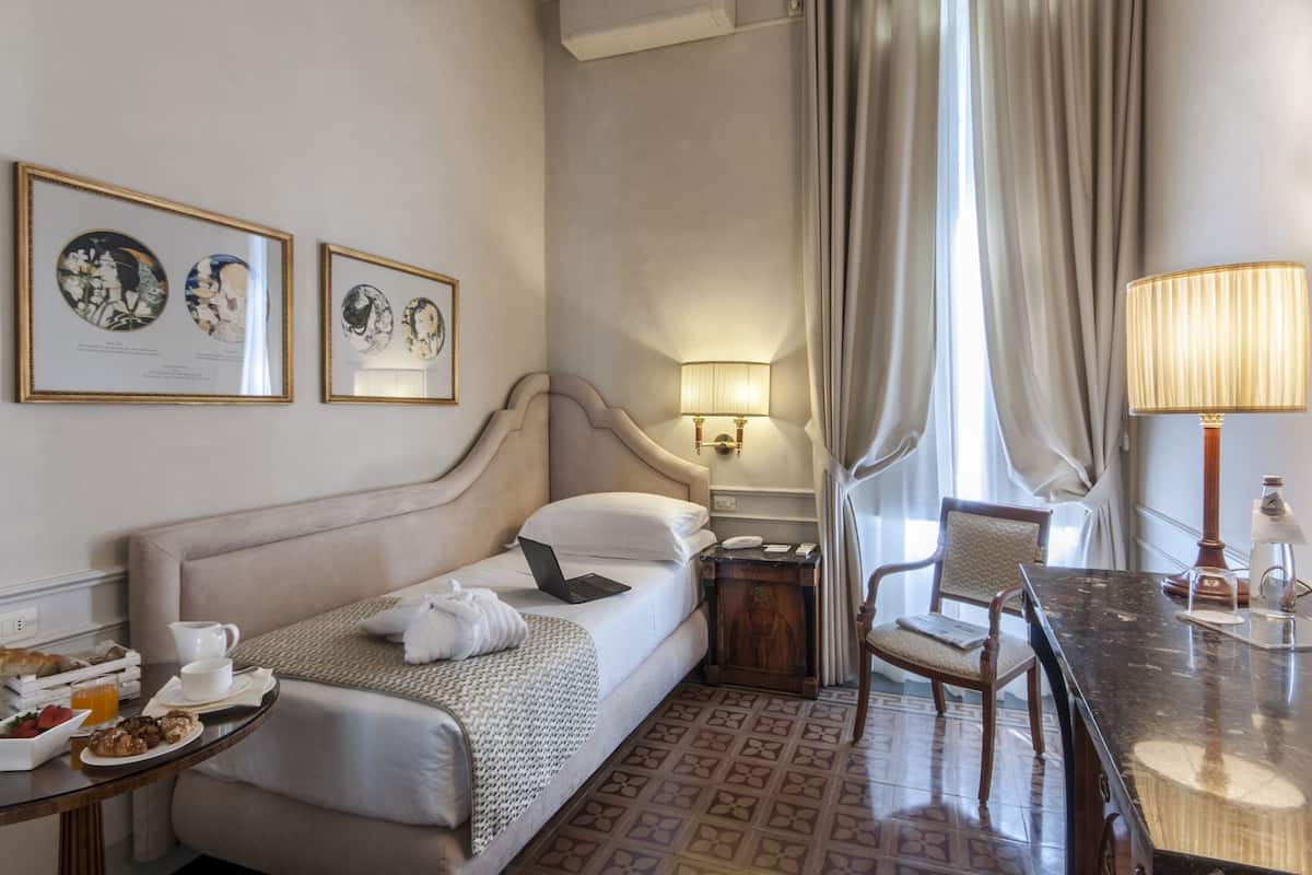 A hotel room with a bed, bedside table, lamp, chair, and breakfast tray.