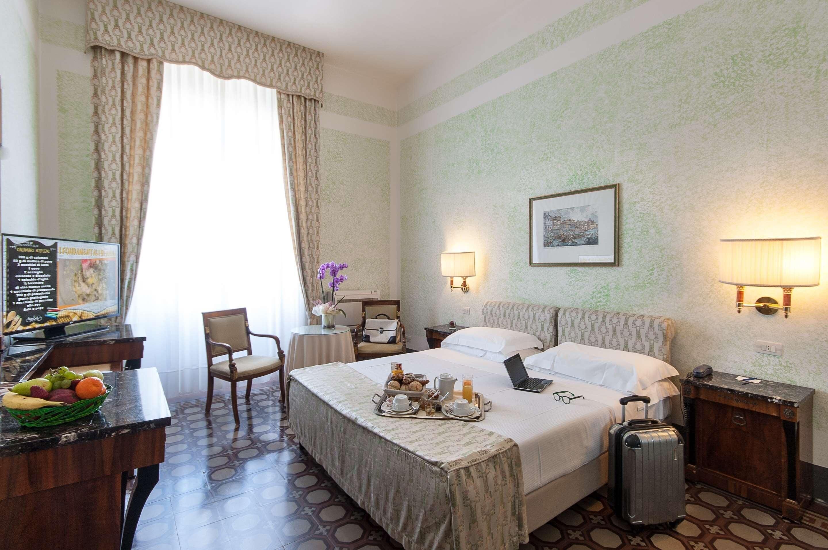Una camera d'albergo con un letto, una scrivania, una sedia, un comodino, una lampada e un quadro appeso al muro.