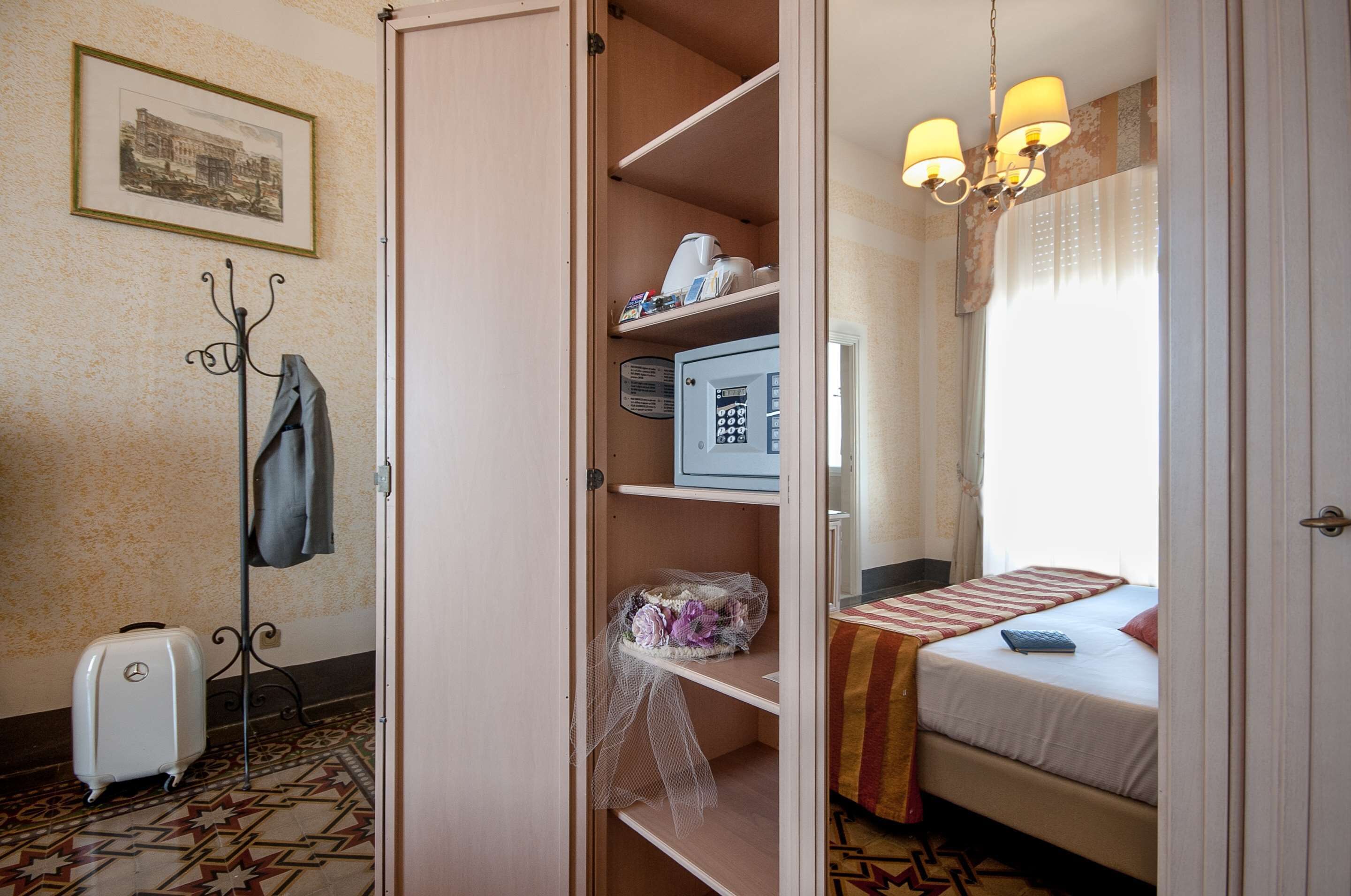 A hotel room with a bed, a desk, a chair, a coat rack, and a suitcase.