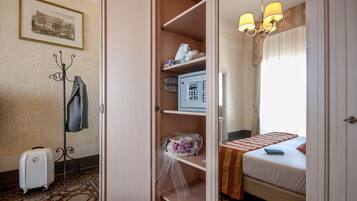 Ein Hotelzimmer mit einem Bett, einem Schreibtisch, einem Stuhl, einem Kleiderhaken und einem Koffer.