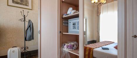 Una habitación de hotel con una cama, un escritorio, una silla, perchero y maleta.