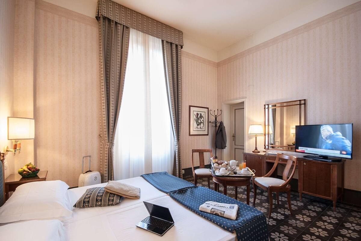 A hotel room with a bed, a desk with a computer, a television, and a dining area with a table and chairs.