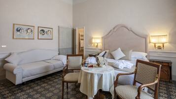 A hotel room with a bed, a sofa, two armchairs, a small round table with a white tablecloth, and two wall-mounted lamps.