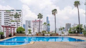 A swimming pool with lounge chairs and potted plants, surrounded by tall buildings and palm trees. - Baiyoke Suite Hotel (Bangkok)