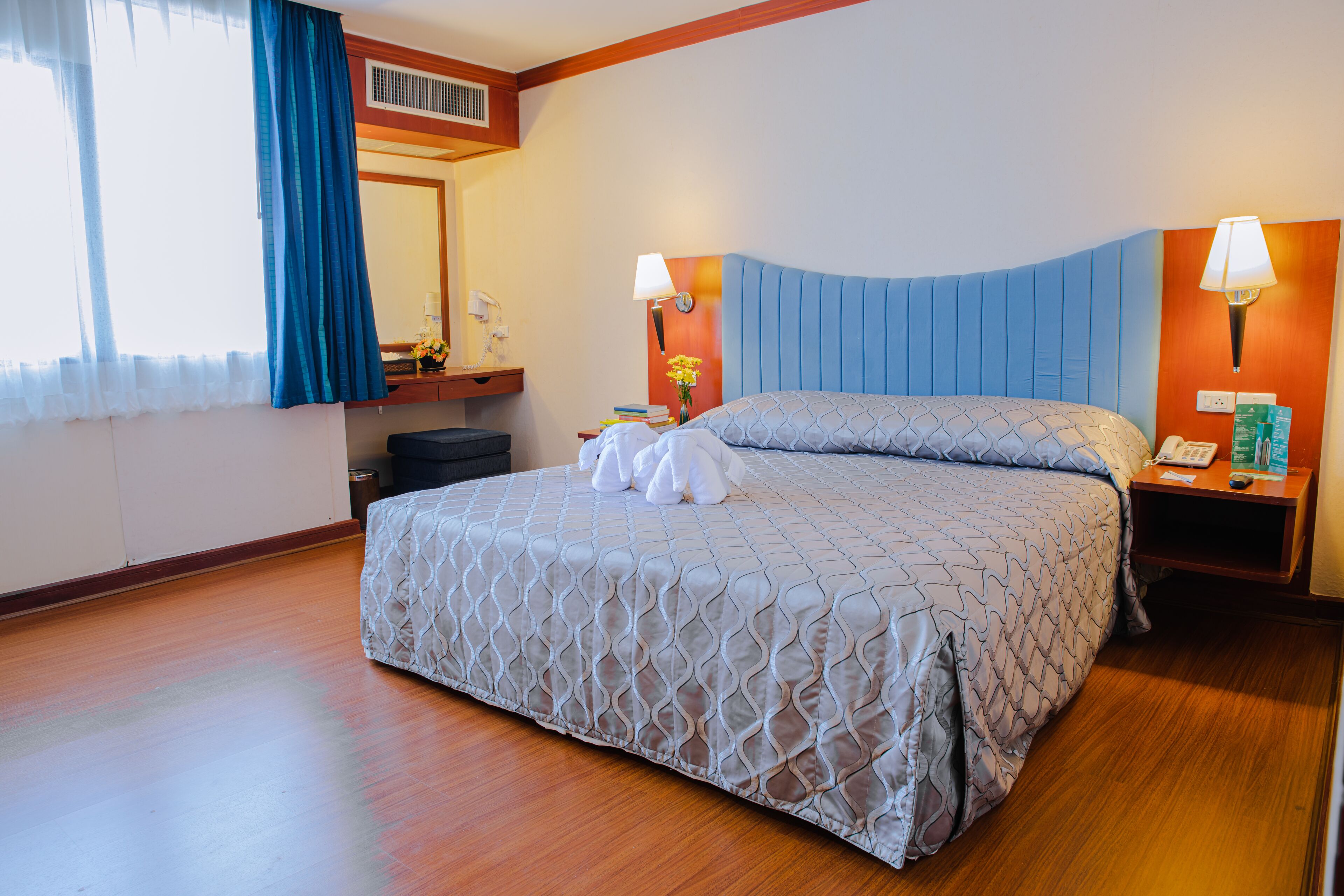 Habitación de hotel con una cama grande, una mesita de noche con lámpara, un teléfono en la mesita y un espejo en la pared.