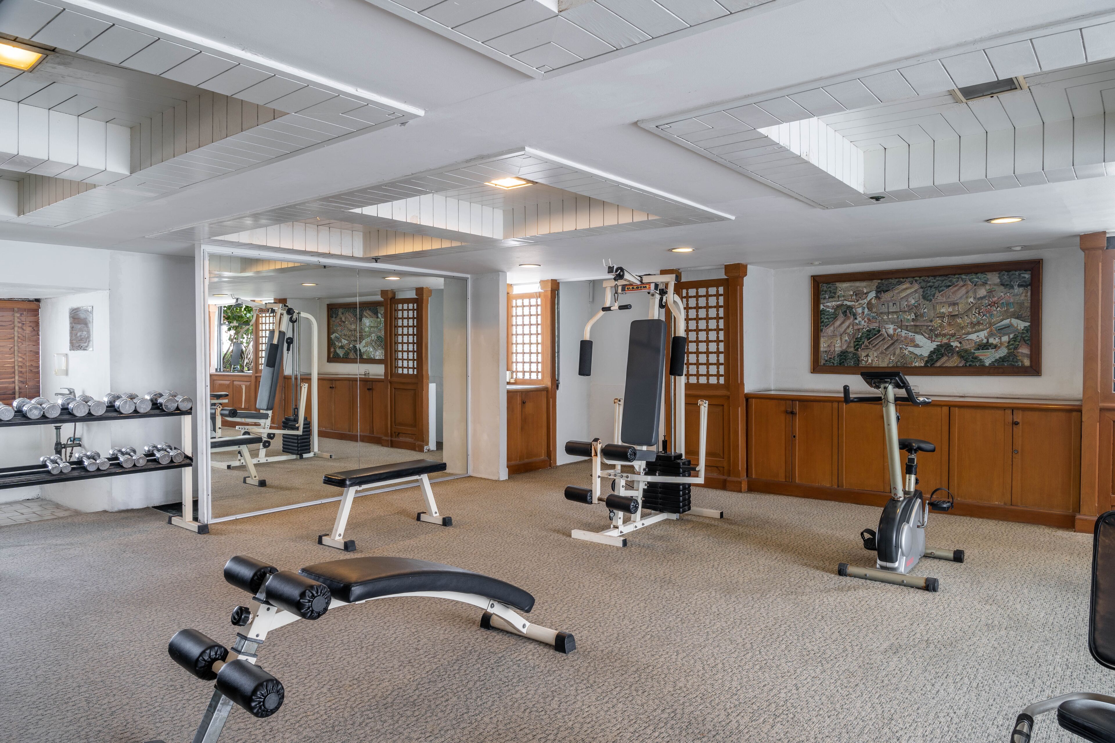 A gym with exercise equipment, a mirror, and a large painting on the wall.