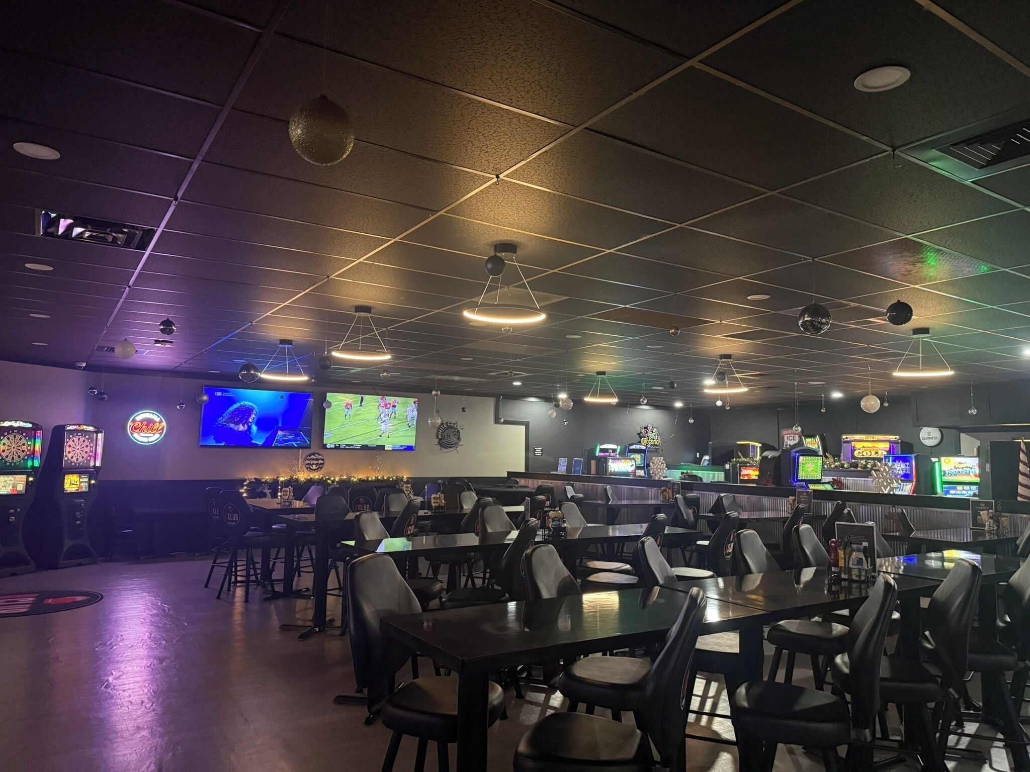 Un espace intérieur à la lumière tamisée, avec des tables et des chaises, des jeux d’arcade et un écran de télévision.