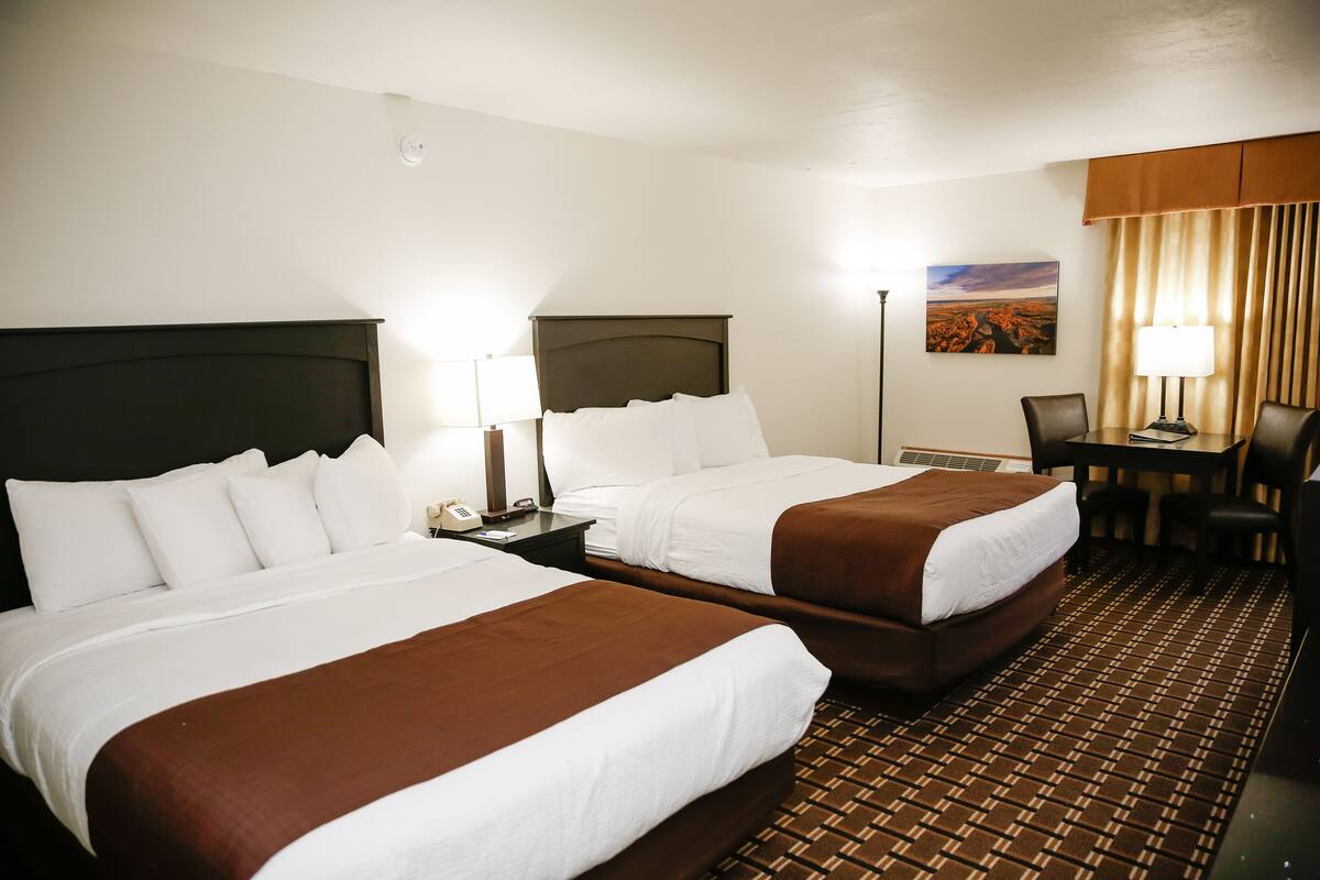 A hotel room with two beds, a desk with a chair, a lamp, and a painting on the wall.