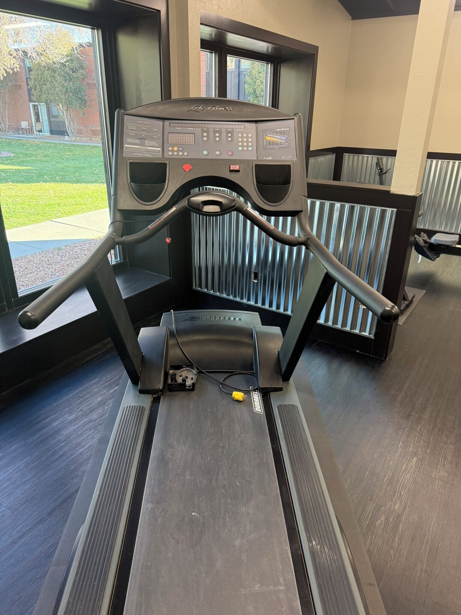 A gym with a treadmill, a control panel, and a view of the outside.