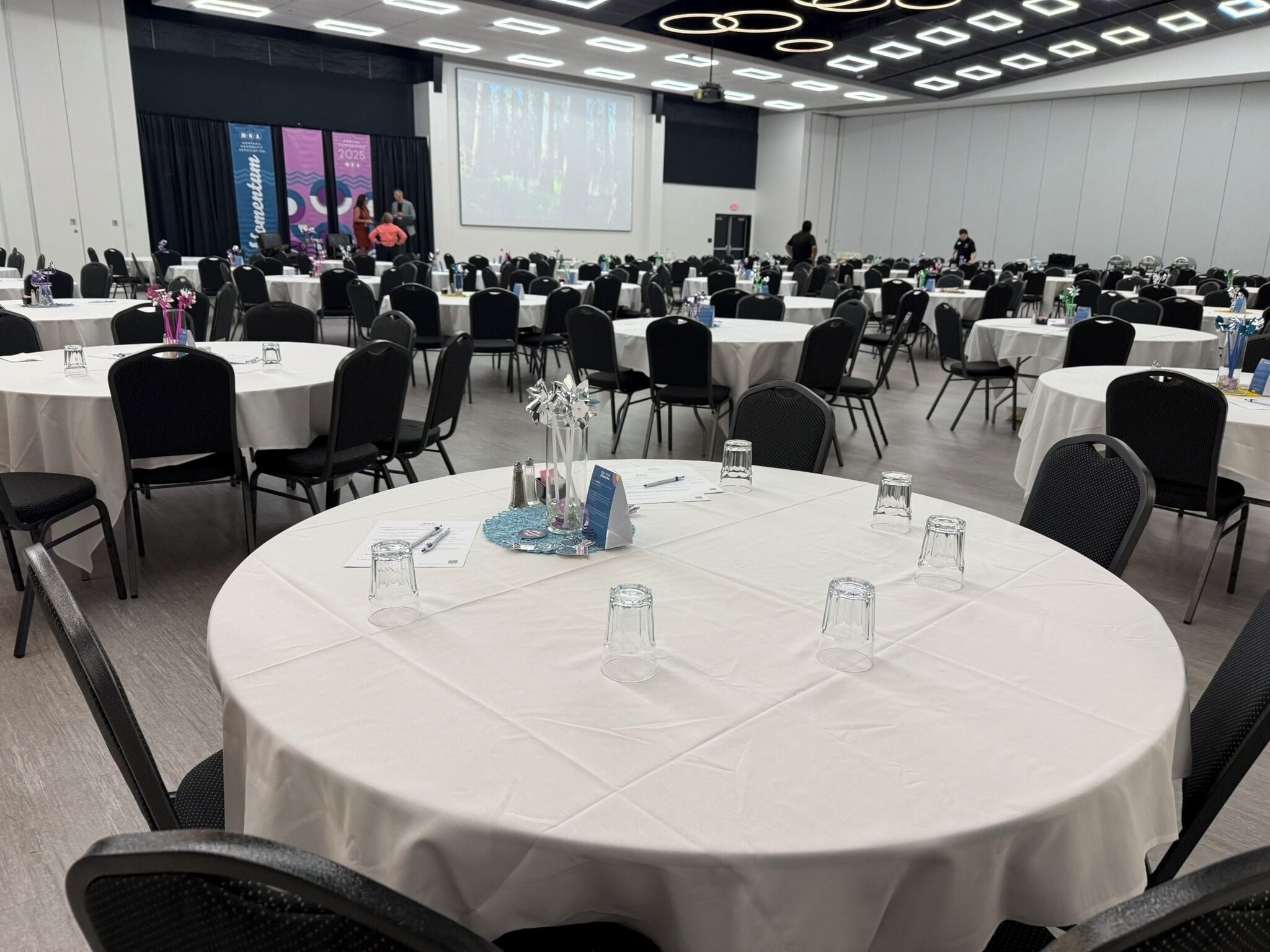 A conference room with round tables, chairs, and a presentation screen.