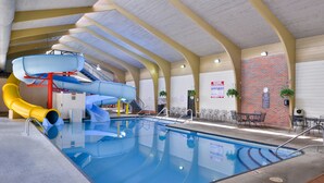 An indoor swimming pool with a water slide and a brick wall with signage.