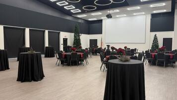 Un salón de conferencias con mesas redondas, manteles negros y posavasos rojos.