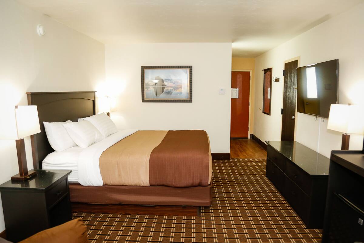 A hotel room with a bed, bedside tables, a mirror, a picture on the wall, and a patterned carpet.