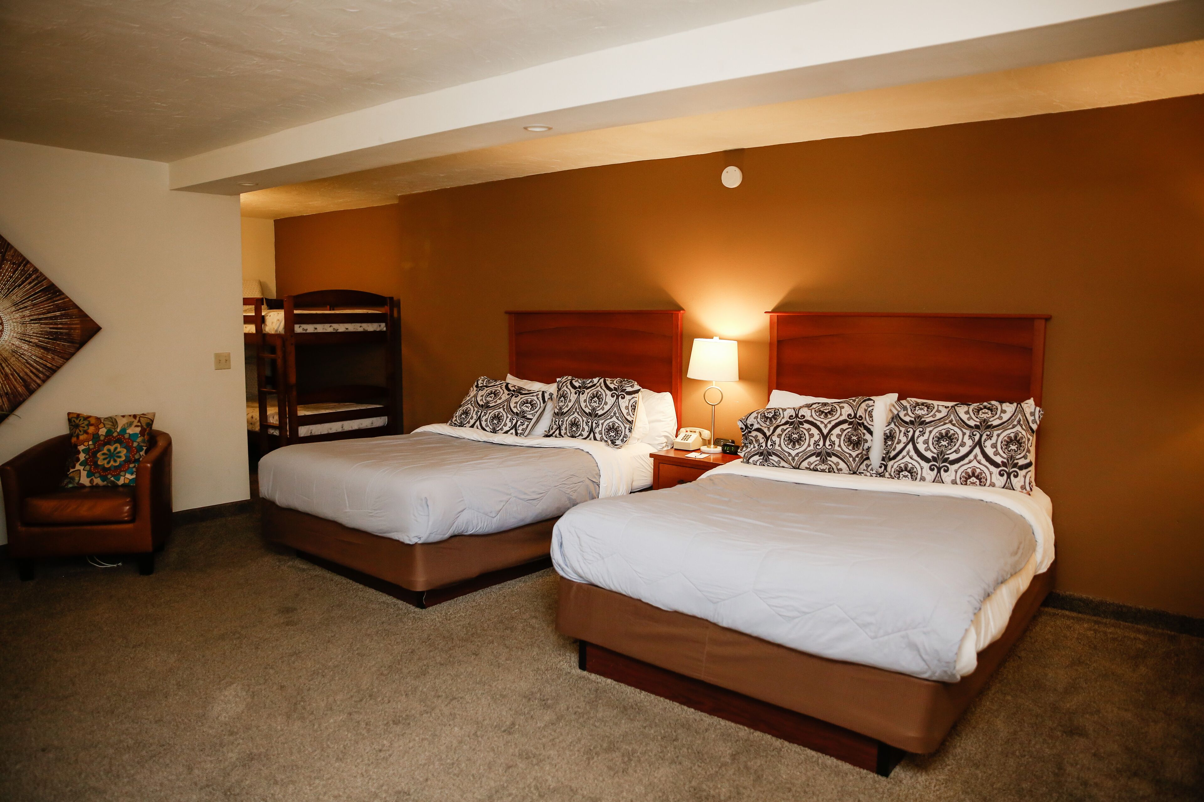 A hotel room with two beds, a nightstand, a lamp, and a chair.