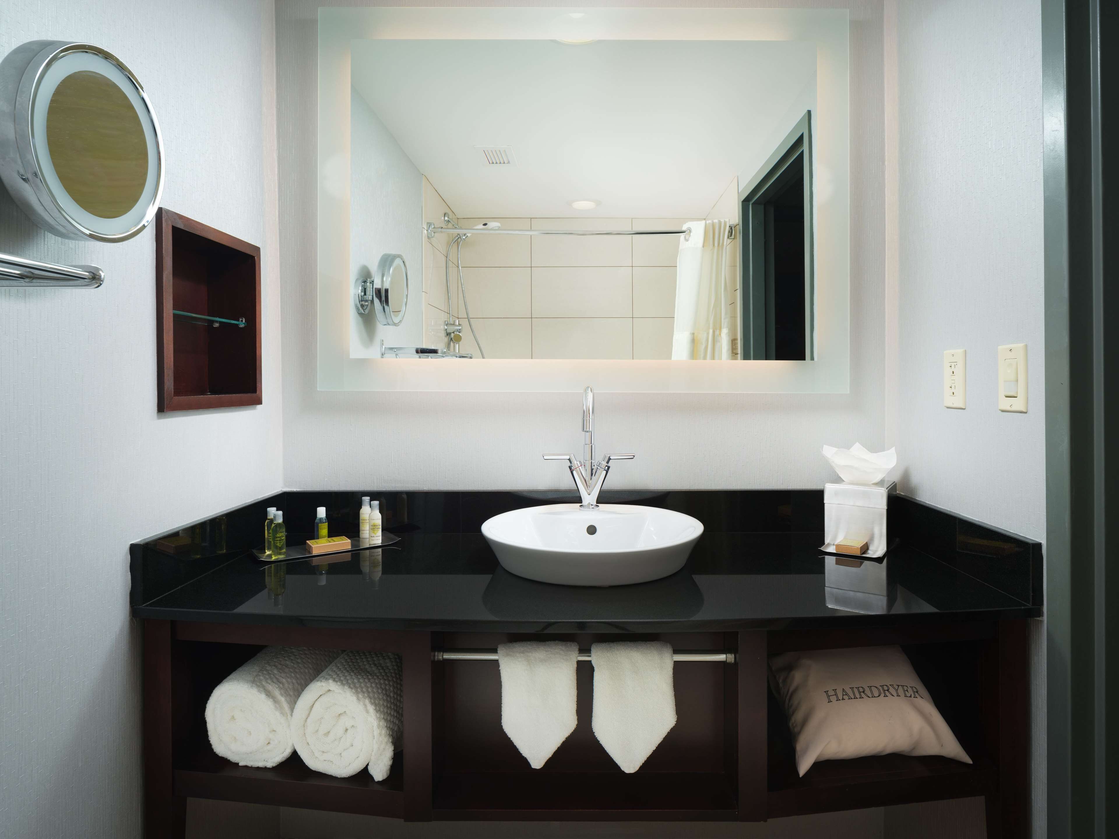 A modern bathroom with a large mirror, a black countertop, a white sink, and a towel rack.