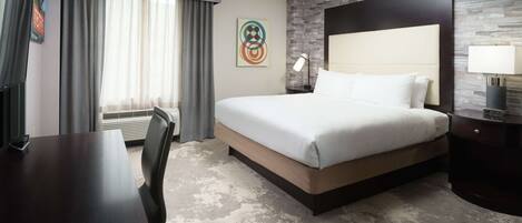 A hotel room with a large bed, a desk, a chair, a lamp, and a wall art piece.