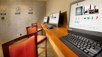 A hotel reception area with a wooden desk, a large ThinkCentre monitor, a keyboard, and two smaller monitors. There are three clocks on the wall and a sign with the hotel's name.