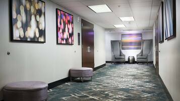 A hotel hallway with a patterned carpet, two armchairs, and artwork on the walls.