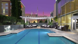 A swimming pool with lounge chairs and a waterfall feature, surrounded by a building with flags and a well-lit exterior. - DoubleTree by Hilton Hotel Chattanooga Downtown (Chattanooga)