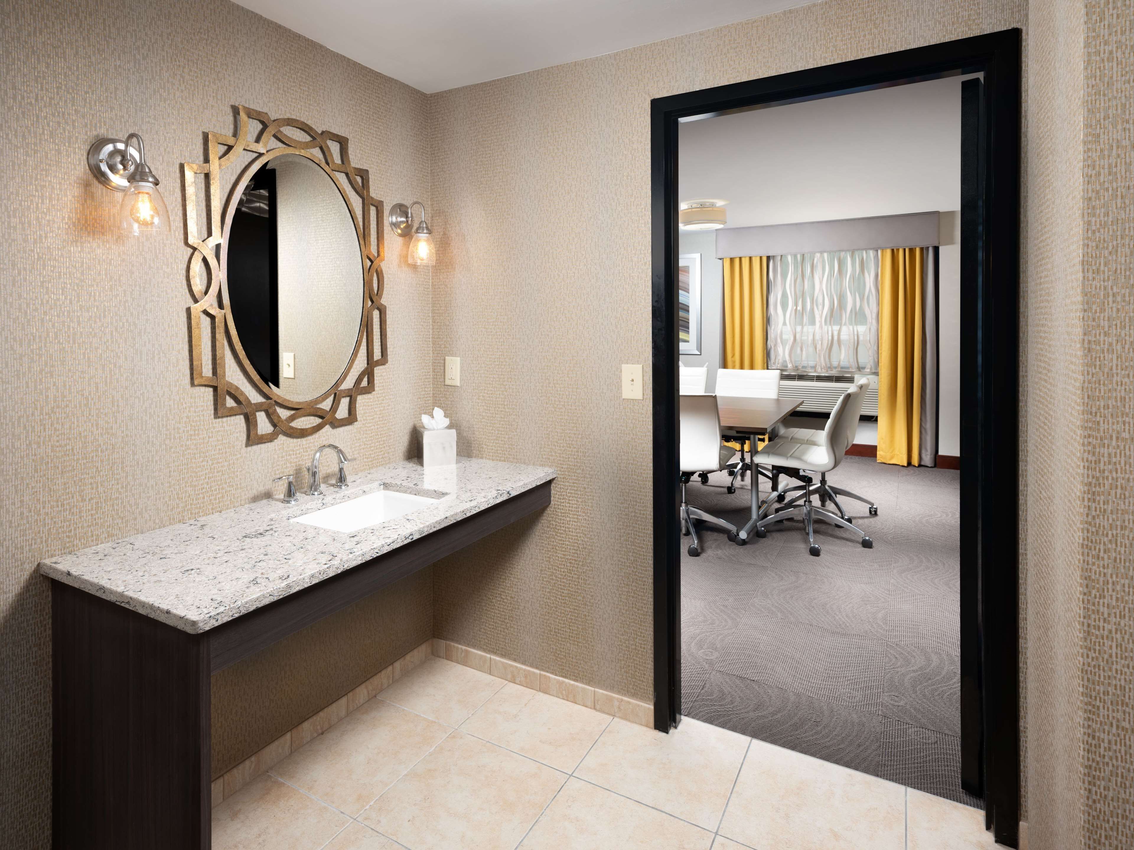 A modern bathroom with a granite countertop, a large mirror, and wall sconces.