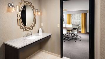 A modern bathroom with a granite countertop, a large mirror, and wall sconces.