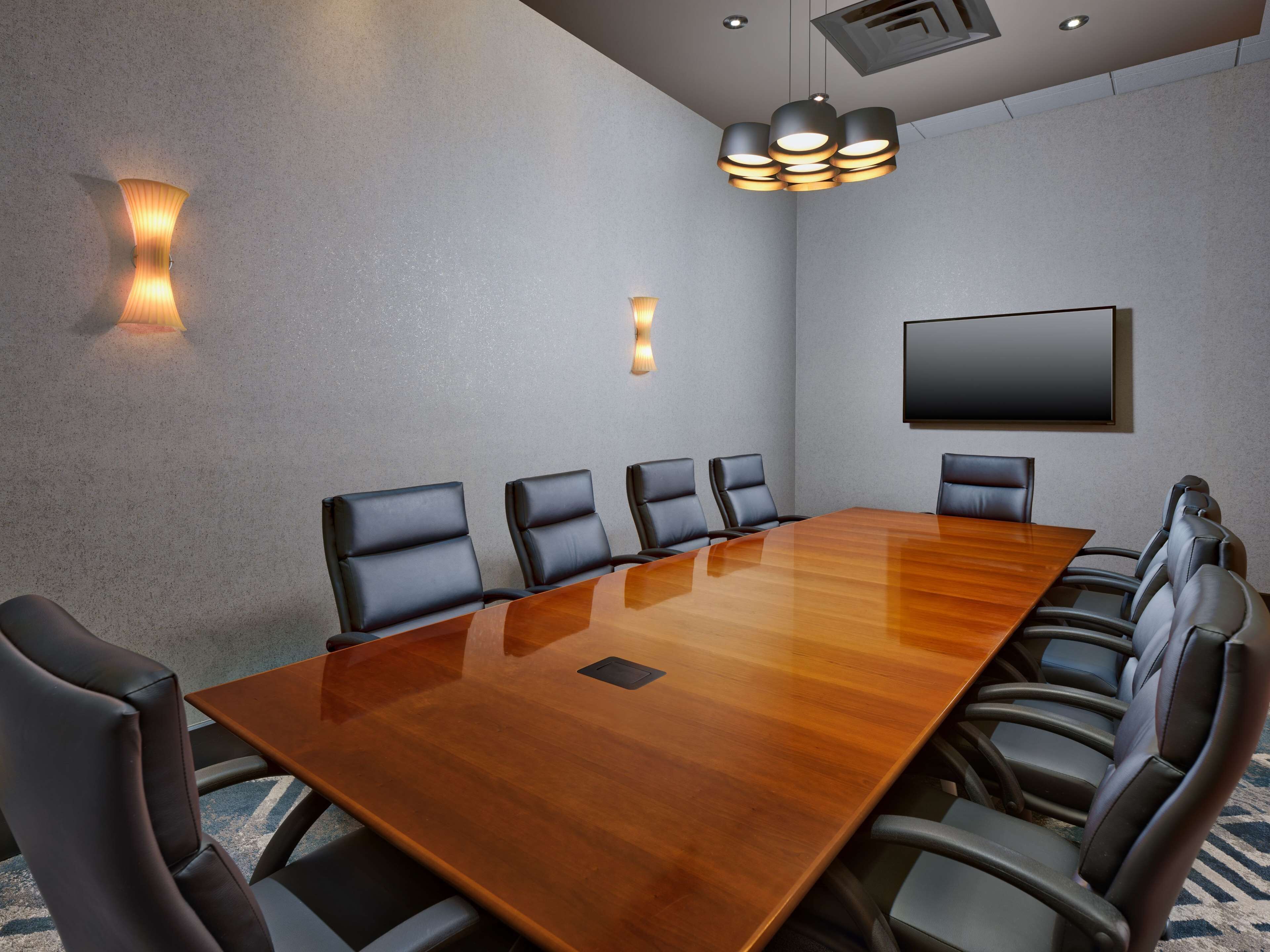 Une salle de conférence dotée d’une grande table en bois, de chaises en cuir noir et d’un éclairage moderne suspendu au plafond.