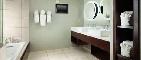 A modern bathroom with two sinks, a large mirror, and a flat-screen TV mounted on the wall.