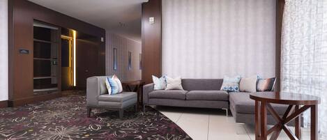 A hotel lobby with a grey sofa set, a wooden coffee table, and a patterned carpet.