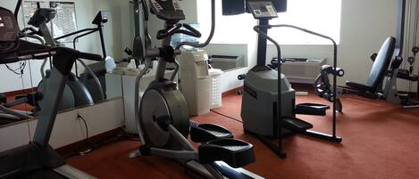 Un gimnasio con diversos equipos de ejercicio, incluyendo cintas de correr, bicicletas estáticas y máquinas de pesas.