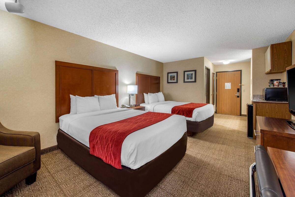 A hotel room with two beds, a desk, a chair, a television, and a microwave.